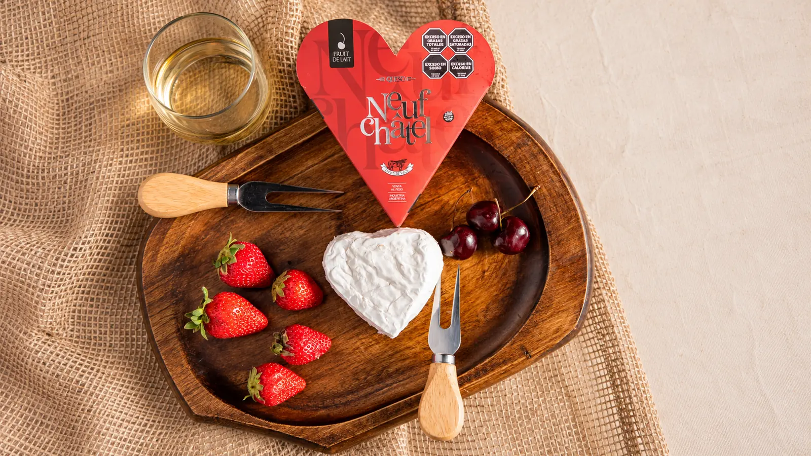 Queso Neufchâtel Fruit de Lait con forma de corazón, sobre tabla de madera con frutillas y cerezas